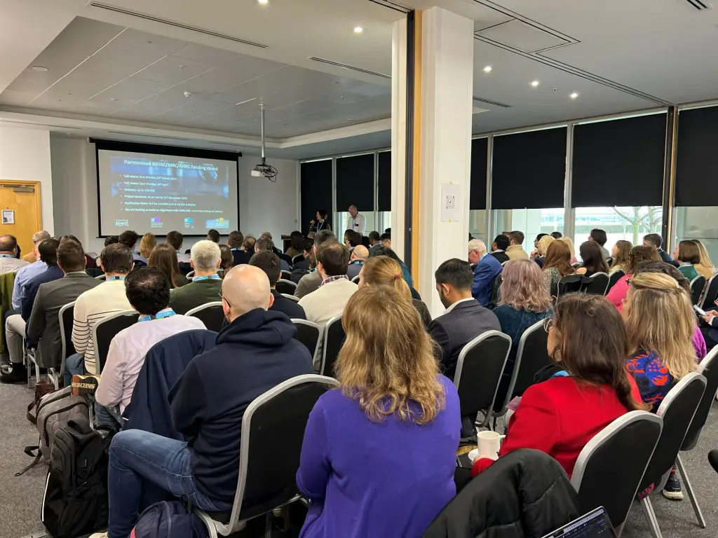 A room of delegates sitting down facing a video screen