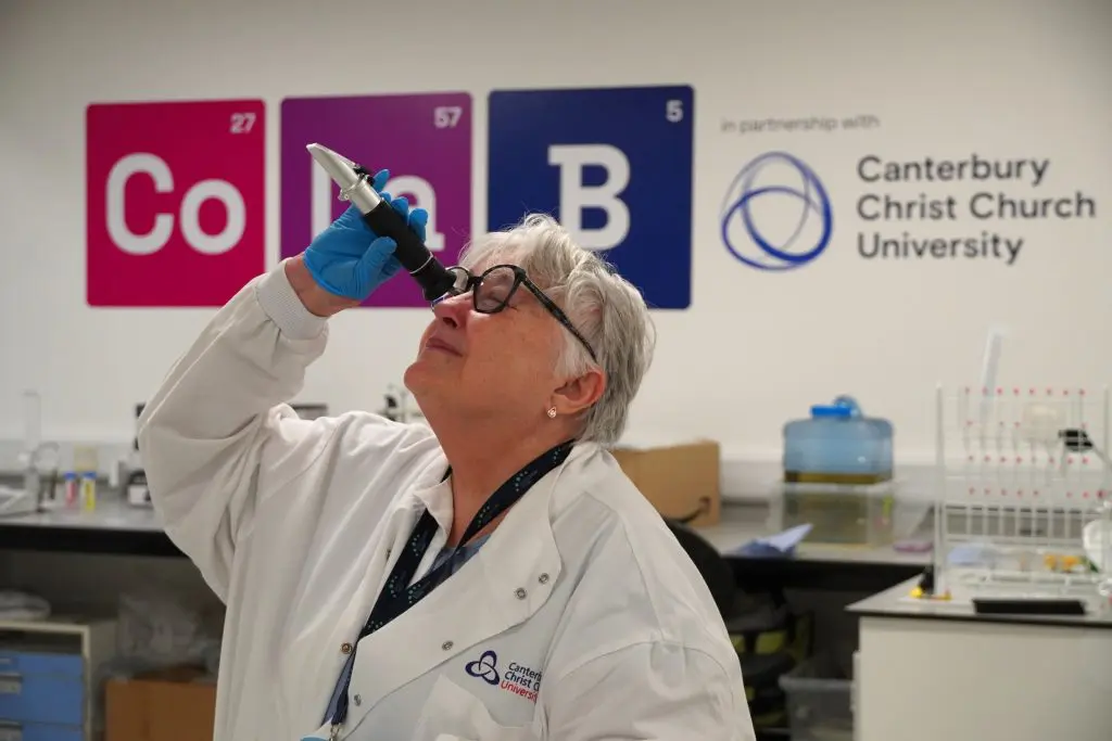 A woman in a lab coat looking through a refractometer